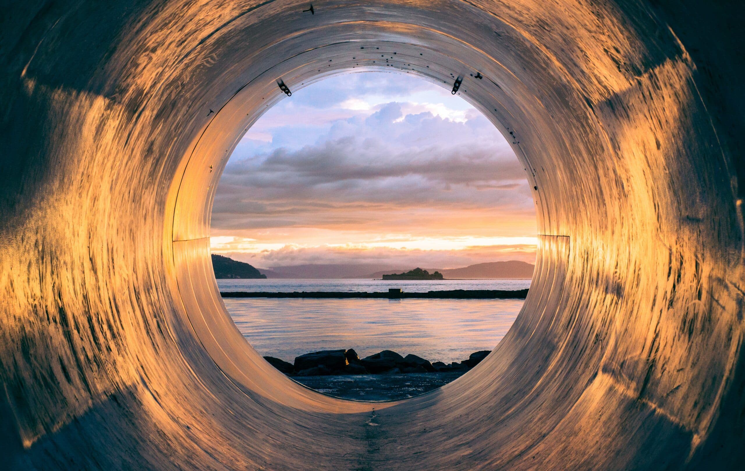 A view of the ocean and shore from inside a pipe.