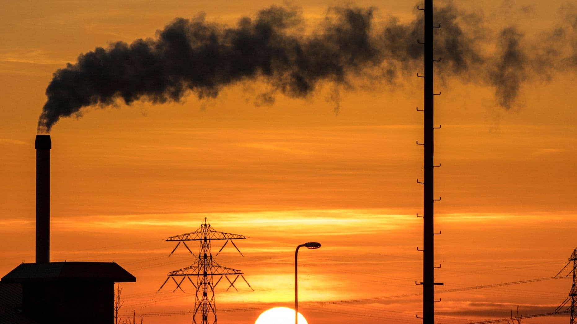 Photo of a sunset with an orange sky, with a factory billowing smoke silhouetted in the foreground.